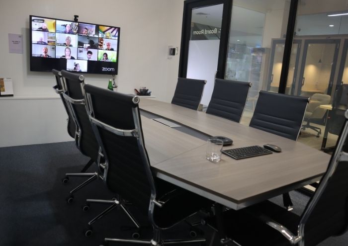 The MSpace boardroom with a seven-seat conference table and a 55-inch display running a video call